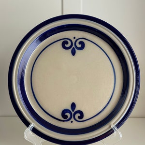 Puede incluir: Un plato de cerámica blanco con un borde azul y diseños florales azules. El plato está en un soporte blanco.