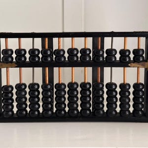 Puede incluir: Un ábaco vintage con marco de madera negra y cuentas negras. Las cuentas están dispuestas en varillas de color cobre. El ábaco tiene esquinas de color latón. Una herramienta clásica para realizar cálculos aritméticos.