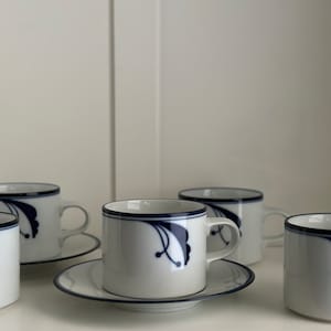 Pode incluir: Conjunto de cinco xícaras de café de cerâmica branca com desenhos florais azuis e pires combinando.