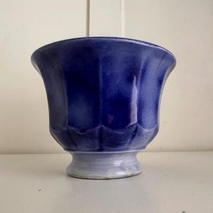 Puede incluir: Una maceta de cerámica azul cobalto con un diseño acanalado. La maceta tiene un borde acampanado y una base azul claro. El interior es de un tono azul más oscuro. La maceta está sobre una superficie blanca.