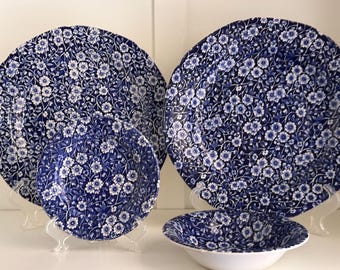 May include: A set of blue and white floral patterned dinnerware, including plates and bowls. The plates are displayed on clear stands, showcasing the intricate floral design. The bowls have a white interior and a blue floral exterior.