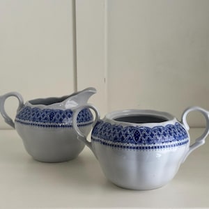 May include: A white creamer and sugar set with blue and white floral designs. The creamer and sugar bowl have a delicate, feminine look.