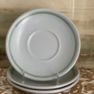 May include: Three white ceramic saucers with a green trim. The saucers are stacked on top of each other.