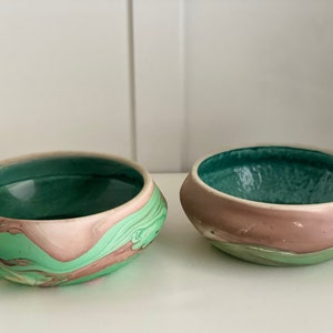 Pode incluir: Duas tigelas de cerâmica com um esmalte verde e rosa marmorizado. As tigelas são redondas e têm uma ligeira borda.