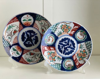 Può includere: Due piatti decorativi in ceramica con un design blu e bianco. I piatti presentano un motivo floreale, forme geometriche e un uccello stilizzato. I piatti sono su supporti da esposizione.