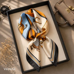 May include: A square silk scarf featuring a horse and equestrian-themed print in shades of light blue, mustard yellow, cream, and black. The scarf is tied in a knot, displaying geometric patterns, striped borders, and the brand name Valzena.