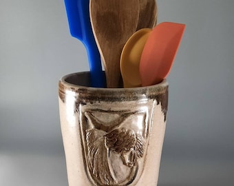 Artisan made kitchen utensil crock, hand carved pine cone and branch on ceramic vase.