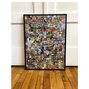 May include: A framed artwork featuring a collage of small, colorful images and text. The images include arrows, the letters "AT", and other symbols. The artwork is displayed on a wooden floor against a white wall.