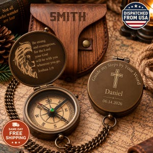 May include: Two antique-style brass pocket compasses with chains. One open compass shows a lion engraving and the text Be strong and courageous, for the Lord your God will be with you wherever you go. Joshua 1:9. The other shows a cross, Daniel, and 06.14.2026.