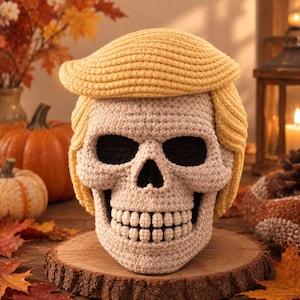 Puede incluir: Una figura de calavera tejida a ganchillo con hilo de color beige claro, con cuencas oculares y cavidad nasal de color negro intenso. La calavera lleva un postizo de hilo amarillo brillante con textura y un flequillo lateral.