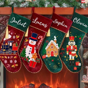 May include: Four velvet Christmas stockings in red and green with gold trim and tassels. Each stocking features a white embroidered name: Juliet, Lucas, Sophia, and Olivia. Designs include a train, a snowman, a gingerbread house, and a nutcracker.