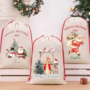 May include: Three beige drawstring Christmas gift sacks with red cords. The left sack features Santa, a snowman, and a reindeer with the text Special Delivery For Aria. The center sack shows a rabbit with the text Hollie Marry Christmas. The right sack displays Santa with the text Special Delivery For Sophia.