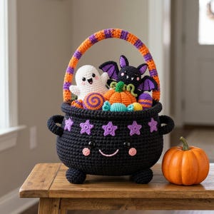 May include: A black crocheted cauldron basket with a smiling face, purple star accents, and a striped orange and purple handle. Inside are crocheted plushies of a white ghost, a black bat, an orange pumpkin, and various colorful candies.