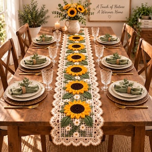 May include: A long, rectangular crochet table runner featuring a repeating pattern of bright yellow sunflowers with dark brown centres and green leaves, bordered by a cream-coloured scalloped lace edge, centred on a wooden dining table.
