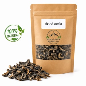 Könnte beinhalten: Ein brauner Papierbeutel mit getrockneten Amla-Stücken und einem Sichtfenster. Das Etikett trägt die Aufschrift "dried amla" und das Logo "HIMALAYAN HERBAL CO." mit einer Berggrafik. Ein grünes, kreisförmiges Emblem mit der Aufschrift "100% NATURAL".