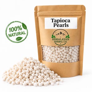 Może przedstawiać: Brązowa torebka stojąca z papieru kraft wypełniona białymi perłami tapioki, z przezroczystym okienkiem i etykietą z napisem Tapioca Pearls oraz Himalayan Herbal Co. Zielona okrągła pieczęć po lewej stronie zawiera tekst 100% NATURAL z ikonami liści.