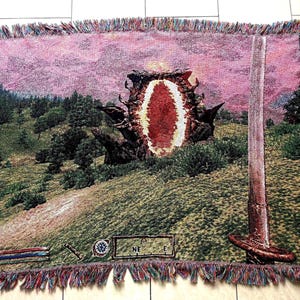 May include: A rectangular woven throw blanket featuring a fantasy landscape with a central glowing portal, a green grassy hill, and a tall sword in the foreground. The bottom edge displays a game-style interface with bars and a compass.