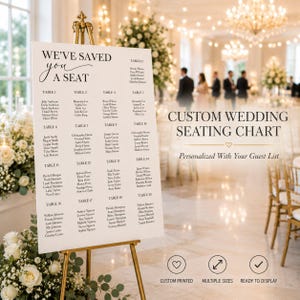 May include: A white wedding seating chart sign on a gold easel featuring the text WE'VE SAVED YOU A SEAT and a list of guest names organized by table numbers. The sign includes the text CUSTOM WEDDING SEATING CHART and Personalized With Your Guest List.