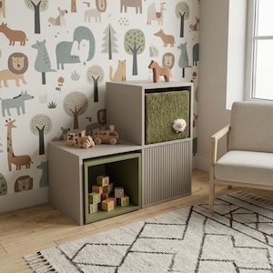 May include: A modular storage unit featuring a light gray frame with two open compartments and one cabinet door with vertical slats. One compartment contains wooden alphabet blocks, while another holds a textured olive green bin with a small sheep plush.