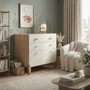 May include: A three-drawer dresser with a light wood frame and off-white drawer fronts. The dresser features small, light-colored knobs and stands on four rounded, light-colored legs. The design is clean and functional, providing storage space.