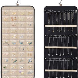 May include: Two hanging jewelry organizers with a metal hook. The left organizer is beige with multiple clear plastic pockets containing various earrings and hair accessories. The right organizer is black with rows of hooks for hanging necklaces.