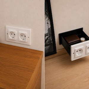 May include: A wall-mounted storage unit featuring a white double electrical outlet faceplate that functions as a drawer front. The interior of the black drawer contains a brown leather wallet and a metallic wristwatch, providing hidden storage space.