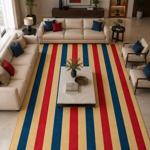 May include: A large rectangular area rug featuring a repeating vertical striped pattern in bold shades of red, deep blue, and light beige. The rug covers the floor space beneath a coffee table and extends between two sofas and two armchairs.