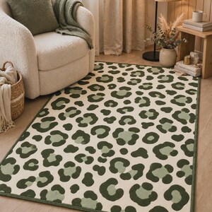May include: A rectangular area rug featuring a repeating leopard print pattern in shades of dark forest green, sage green, and cream. The rug has a finished bound edge in a matching dark green color and a low-pile texture across the entire surface.