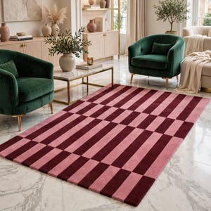 May include: A rectangular area rug featuring a geometric pattern of alternating vertical stripes in deep burgundy and soft dusty pink. The rug has a low-pile texture and covers a portion of the floor, displaying a consistent repeating color block design.