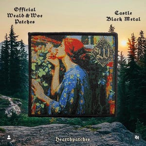 May include: A square embroidered patch featuring a person with long red hair wearing a blue patterned garment, surrounded by colourful flowers and foliage. A diamond-shaped logo with the letters SW is in the upper right corner. The border is black.