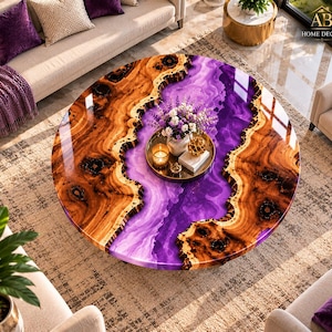 May include: A round coffee table featuring a natural wood slab with a live edge and a central river of vibrant purple resin. A gold circular tray sits on the surface, holding a small vase of purple flowers, a candle, and a decorative object.