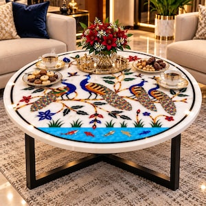 May include: A round white marble coffee table with a black metal base. The tabletop features an intricate inlay design of three peacocks perched on branches, surrounded by floral motifs and a blue water border with colourful fish swimming inside.