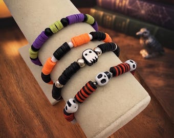 May include: Four stretch bracelets featuring colourful polymer clay heishi beads. The designs include purple, lime green, orange, and black segments, accented with silver-toned spacers and white beads shaped like ghosts and skulls.