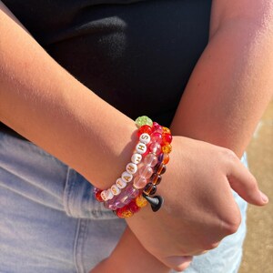 May include: A stack of three beaded bracelets featuring a variety of colorful translucent and opaque beads. One bracelet includes white letter beads spelling out the word "STAHHS" in black text, while another features a small black charm.