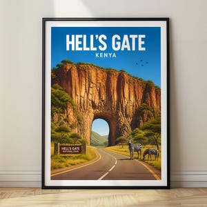 May include: A framed travel poster featuring a landscape of Hell's Gate National Park in Kenya. The artwork displays a tall rock formation with a natural archway, a paved road, two zebras, and a park sign. The sky is blue with small birds.