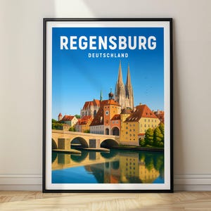 Può includere: Un poster di viaggio incorniciato della città di Regensburg, Deutschland. L'illustrazione raffigura un ponte in pietra su un fiume con un paesaggio urbano storico, inclusa una cattedrale con due guglie e edifici dai tetti arancioni.