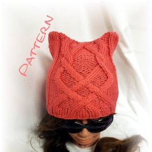 May include: A coral pink knitted hat with cat ears and a cable knit pattern.