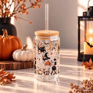 Puede incluir: Un vaso de vidrio transparente con tapa de bambú y pajita de vidrio, que presenta un patrón repetitivo de fantasmas blancos, calabazas negras y naranjas, sombreros de bruja, lunas crecientes, murciélagos y pequeños elementos florales.