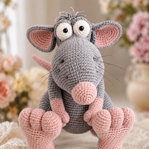 May include: A crocheted stuffed animal shaped like a rat with gray yarn for the body, pink yarn for the large feet, hands, nose, and inner ears, and two large white circular eyes with black pupils. The rat has thin black whiskers on its snout.