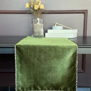 Peut inclure: Un chemin de table rectangulaire en velours vert olive uni. Le chemin de table présente une bordure étroite avec un motif imprimé léopard noir et blanc sur les quatre côtés, offrant un contraste marqué avec le centre en velours vert doux.