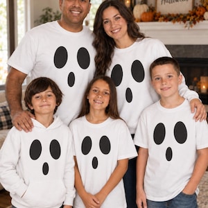 May include: A collection of white shirts and sweatshirts featuring a black ghost face graphic with two oval eyes and a smaller oval mouth. The garments include a mix of short-sleeve t-shirts and long-sleeve hooded sweatshirts, all displaying the same ghost design.