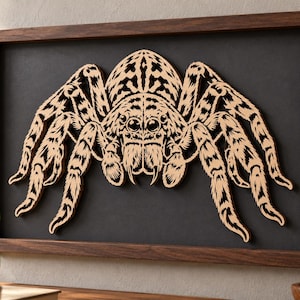 May include: A rectangular wall art piece featuring a light-colored, laser-cut wooden spider with intricate, dark-etched patterns on its body and eight legs, mounted against a solid black background inside a dark brown wooden frame.