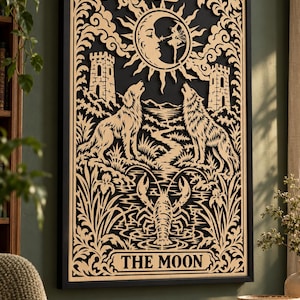 May include: A rectangular wall art piece featuring a laser-cut wooden design of The Moon tarot card in a black frame. The light wood cutout depicts a crescent moon with a face, two howling wolves, a lobster, and two towers on a black background.