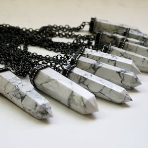 May include: A silver chain necklace with multiple white howlite crystal pendants. Each pendant is a long, pointed, and faceted crystal with a silver cap at the top.