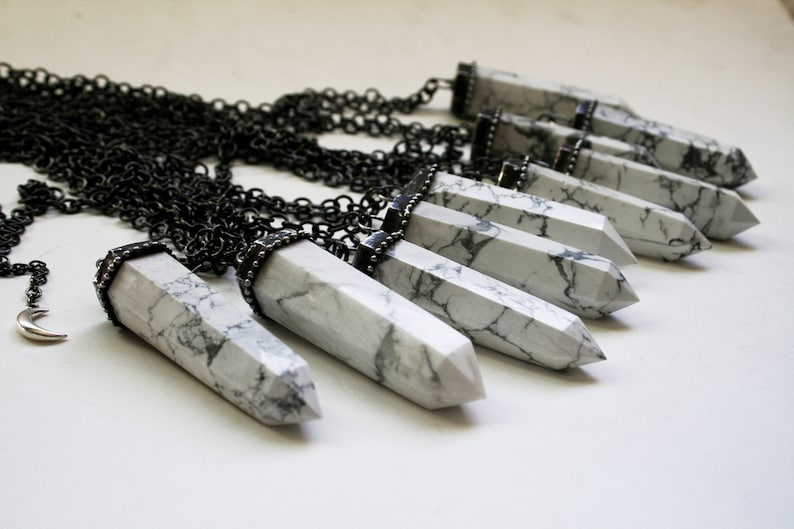 May include: A silver chain necklace with multiple white howlite crystal pendants. Each pendant is a long, pointed, and faceted crystal with a silver cap at the top.