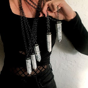 May include: A layered necklace with multiple silver chains and white crystal pendants. The crystals are long and pointed, resembling a tower or obelisk shape.