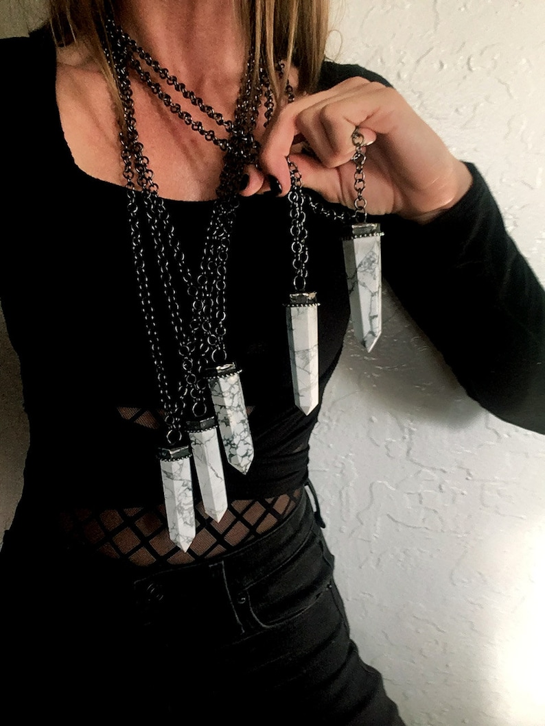 May include: A layered necklace with multiple silver chains and white crystal pendants. The crystals are long and pointed, resembling a tower or obelisk shape.