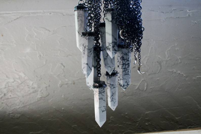 May include: A collection of white, marbled, crystal-shaped pendants hang from a black chain. The pendants are all different sizes and shapes, and they are connected to the chain by silver rings.