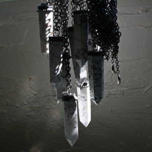 May include: A collection of white crystal pendants hanging from black chains. The crystals are all different shapes and sizes, and they are all attached to a single chain.