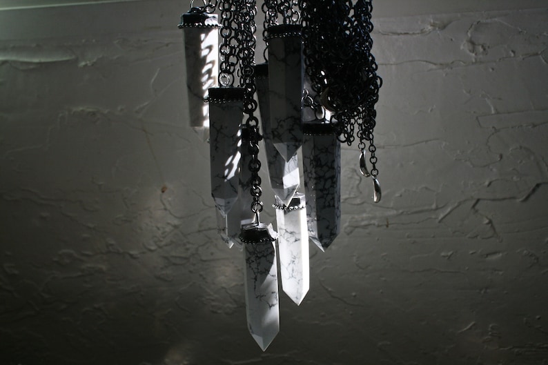 May include: A collection of white crystal pendants hanging from black chains. The crystals are all different shapes and sizes, and they are all attached to a single chain.